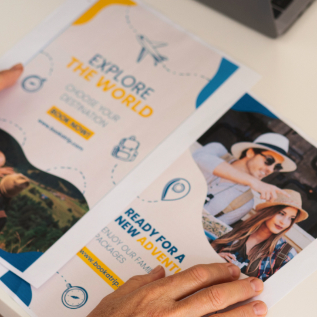 Two travel brochure flyers lying on a table with the hands of a woman resting on it