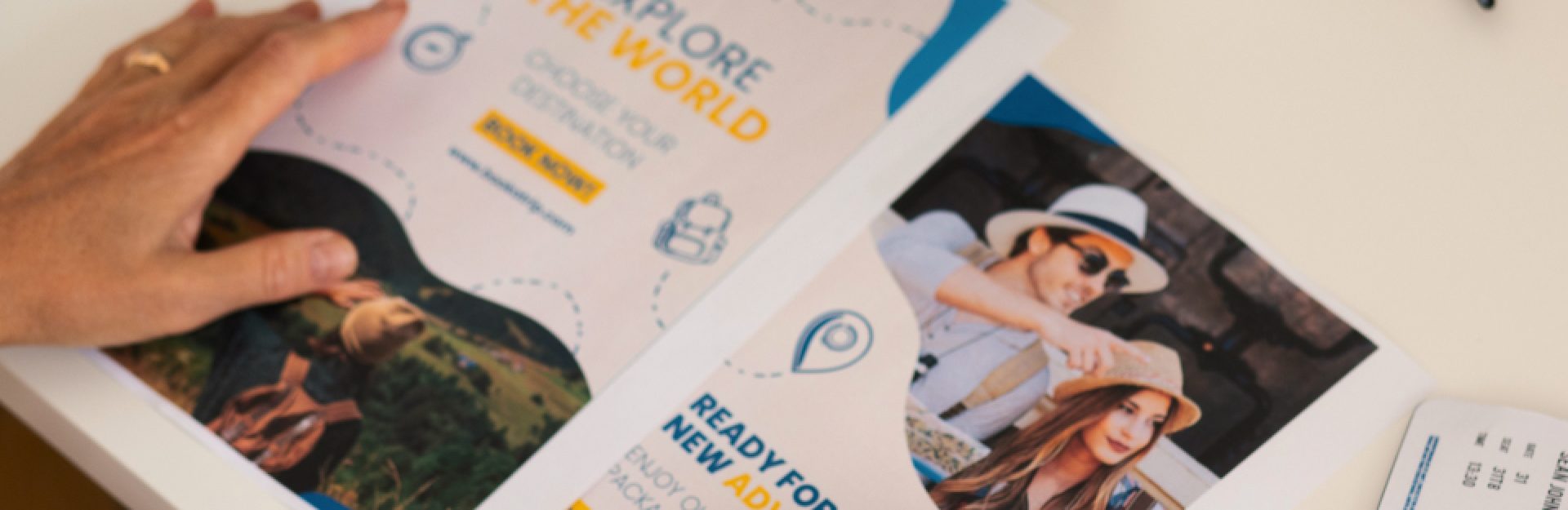 Two travel brochure flyers lying on a table with the hands of a woman resting on it
